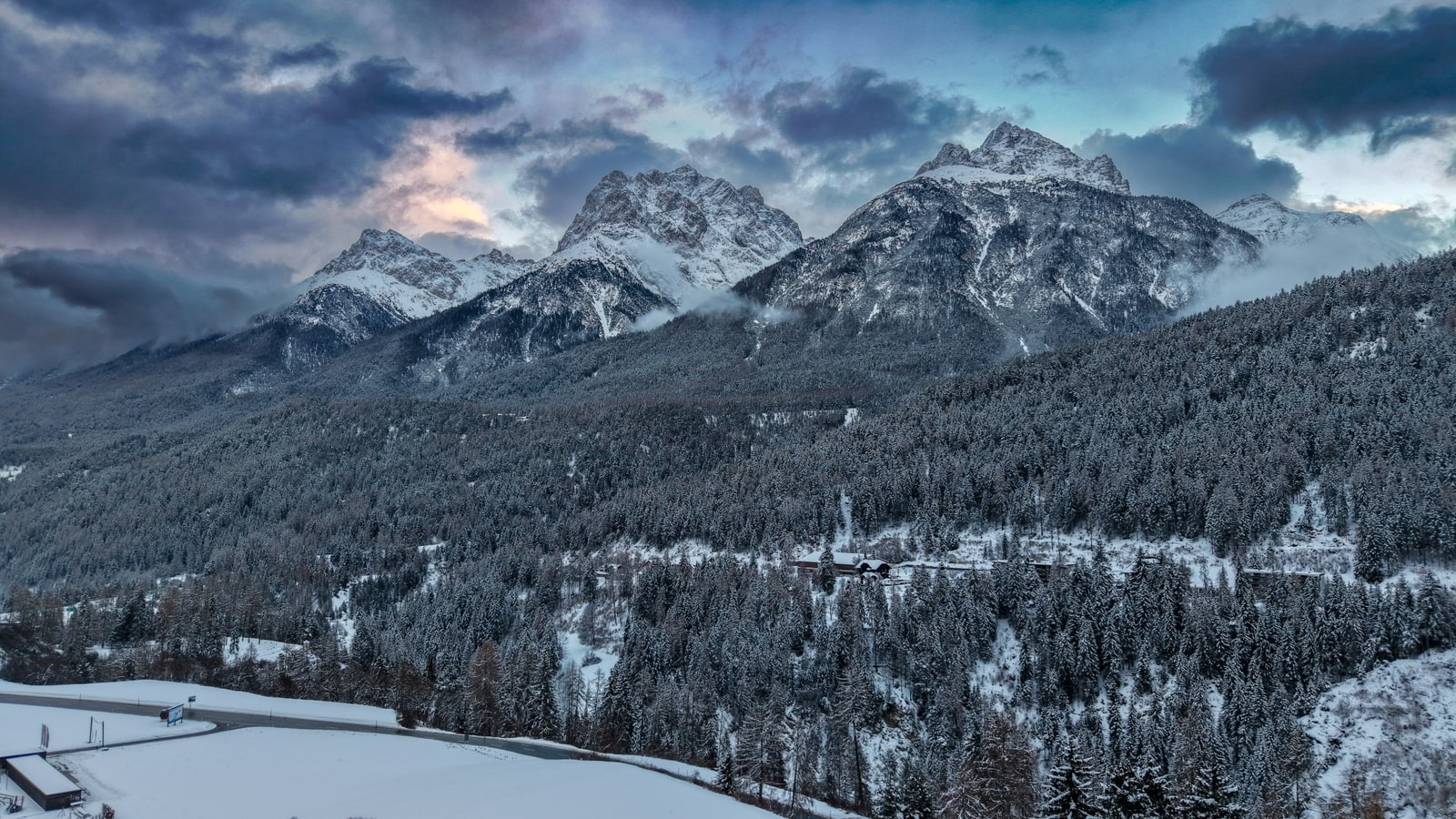 Aerial view of pristine winter landscape in Switzerland with snow-covered valley and frozen river winding through alpine terrain
